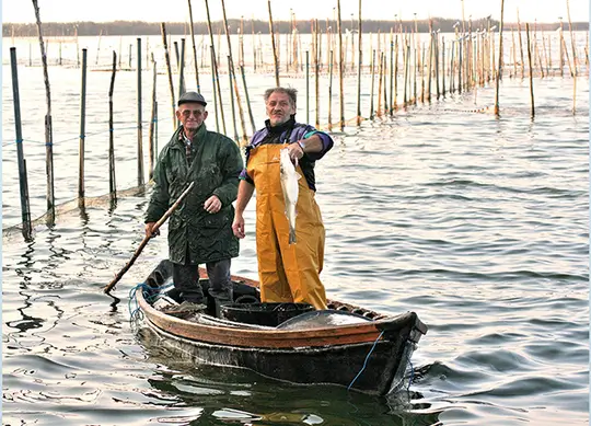 Una dona i un home pescant en barca entre estaques